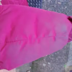 Fragment rękawa różowej kurtki puchowej z widocznymi zagnieceniami i lekkim zabrudzeniem.