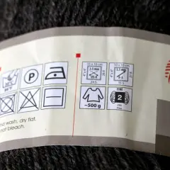Etykieta na motku ciemnej włóczki z symbolami pielęgnacji i informacją o wadze (~500g).