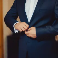 Mężczyzna zapina elegancki, granatowy **strój formalny**. Widać białą koszulę i mankiet z francuskimi spinkami.