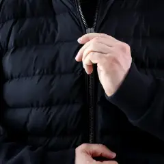Ręce zapinają zamek w czarnej, pikowanej kurtce. Dowiedz się, jak naprawić zamek w kurtce, gdy się zacina.