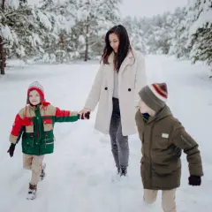 Mama z dwójką dzieci w zimowym lesie. Podpowiadamy, jak ubrać dziecko pod kombinezon, by było mu ciepło i wygodnie na sankach.