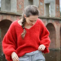 Kobieta w czerwonym swetrze z moheru i w kratę, na tle ceglanych arkad.