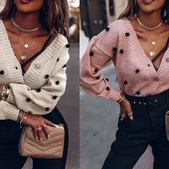 Dwie kobiety w swetrach z pomponami. Pokazują, jak zapiąć sweter na guziki, tworząc stylowy, warstwowy look.