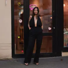 Elegancka kobieta w czarnym, głęboko wyciętym kombinezonie. Idealna inspiracja, co założyć do czarnego kombinezonu na wieczór.