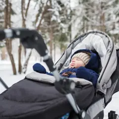 Śpiące dziecko w wózku, ubrane w ciepły kombinezon zimowy, czeka na spacer.