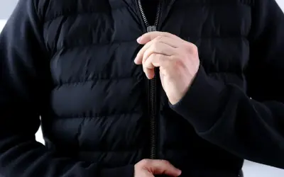 Ręce zapinają zamek w czarnej, pikowanej kurtce. Dowiedz się, jak naprawić zamek w kurtce, gdy się zacina.