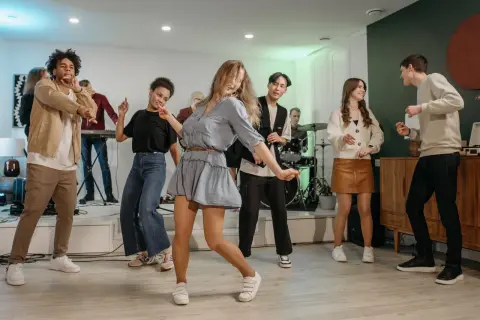 Luźne stylizacje na domówkę: jeansy, sukienki i wygodne buty. Bawiący się ludzie w różnorodnych strojach.