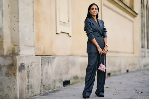 Elegancka kobieta w garniturze w **gołębi kolor** i różową torebką na łańcuszku.
