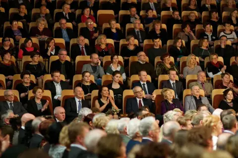 Elegancko ubrani widzowie siedzą w teatrze, gotowi na spektakl. To inspiracja, jak się ubrać do teatru.