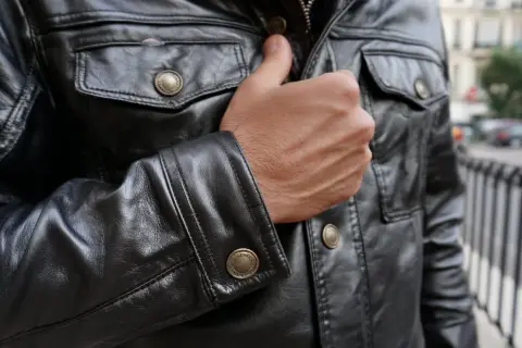 Mężczyzna w czarnej, skórzanej kurtce z ozdobnymi guzikami. Kto przerabia kurtki skórzane? Ten styl to klasyka.