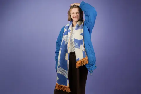 Dziewczyna w niebieskiej kurtce z kapturem i wzorzystym szaliku. Pokazuje, jak nosić szalik do kurtki z kapturem, tworząc stylowy look.