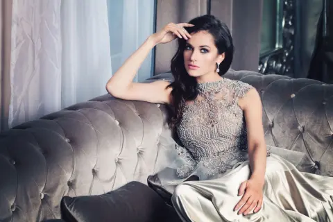 Elegancka kobieta w sukni zdobionej kryształkami, siedząca na aksamitnej kanapie. To uosobienie tego, co znaczy glamour.