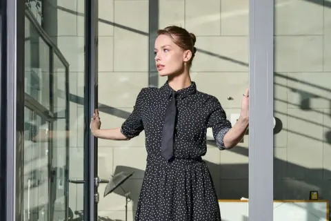 Elegancka sukienka w kropki z krawatem – idealna na imprezę firmową. Kobieta wchodzi przez szklane drzwi.