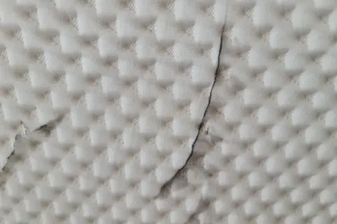Biała tkanina z pikowanym wzorem i ciemnymi smugami.