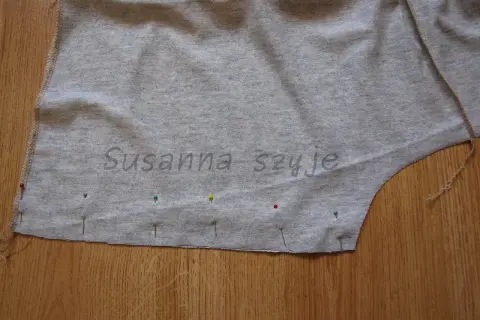 Szara tkanina bluzki z naszytymi szpilkami, gotowa do zwężenia pod pachami.