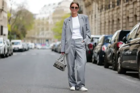 Elegancki damski garnitur w stylu smart casual, biały top, sneakersy i torebka Fendi.