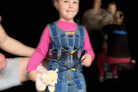 Uśmiechnięta dziewczynka w niebieskim kombinezonie Dunag, trzymająca misia. Gdzie kupić taki kombinezon?