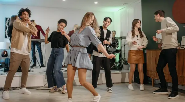 Luźne stylizacje na domówkę: jeansy, sukienki i wygodne buty. Bawiący się ludzie w różnorodnych strojach.