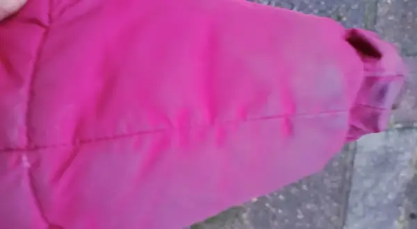 Fragment rękawa różowej kurtki puchowej z widocznymi zagnieceniami i lekkim zabrudzeniem.