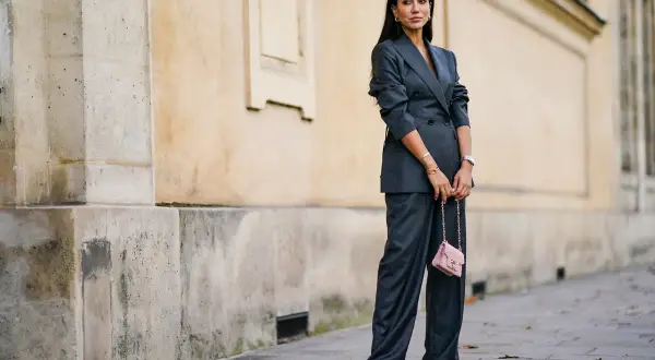 Elegancka kobieta w garniturze w **gołębi kolor** i różową torebką na łańcuszku.