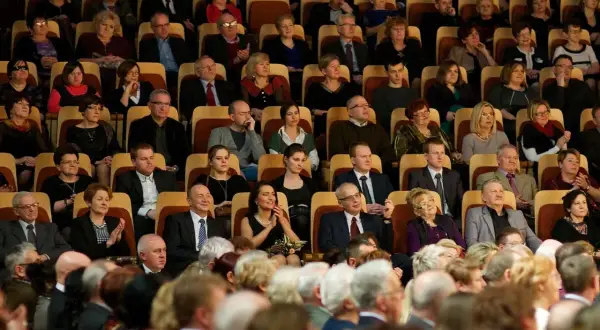 Elegancko ubrani widzowie siedzą w teatrze, gotowi na spektakl. To inspiracja, jak się ubrać do teatru.
