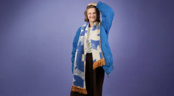 Dziewczyna w niebieskiej kurtce z kapturem i wzorzystym szaliku. Pokazuje, jak nosić szalik do kurtki z kapturem, tworząc stylowy look.
