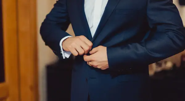 Mężczyzna zapina elegancki, granatowy **strój formalny**. Widać białą koszulę i mankiet z francuskimi spinkami.