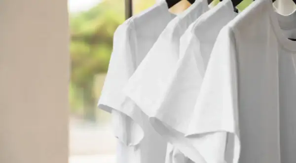 Białe bluzki wiszące na wieszakach. Chcesz wiedzieć, jak odplamić białą bluzkę? Te czyste koszulki czekają na pranie.