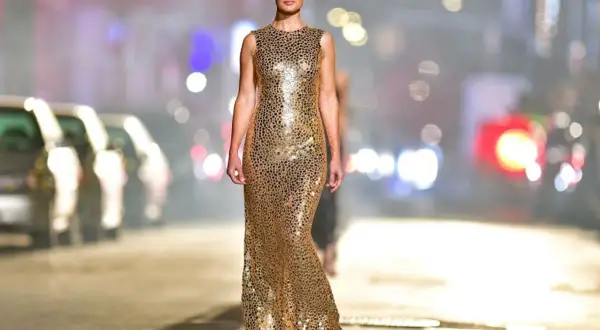 Modelka w złotej, cekinowej sukience na wybiegu. Jakie buty do złotej cekinowej sukienki? Eleganckie szpilki lub sandałki na obcasie.
