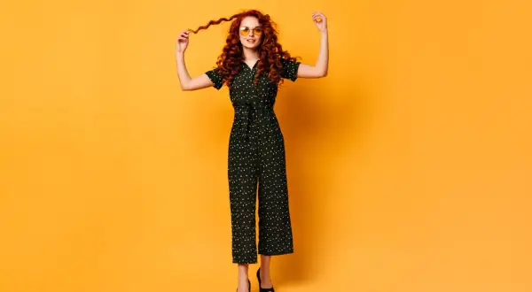 Kobieta w czarnym kombinezonie w groszki i okularach przeciwsłonecznych.