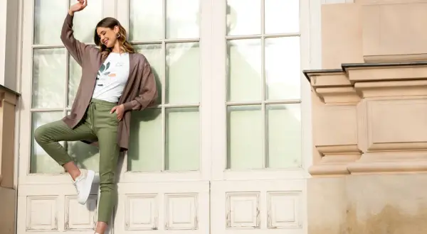 Elegancka kobieta w brązowym kardiganie i zielonych spodniach pokazuje, jak nosić kardigan na co dzień.