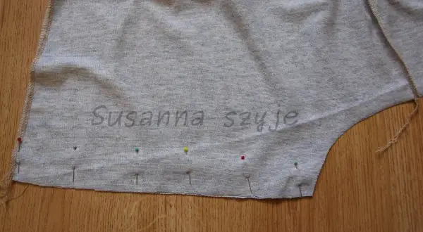 Szara tkanina bluzki z naszytymi szpilkami, gotowa do zwężenia pod pachami.