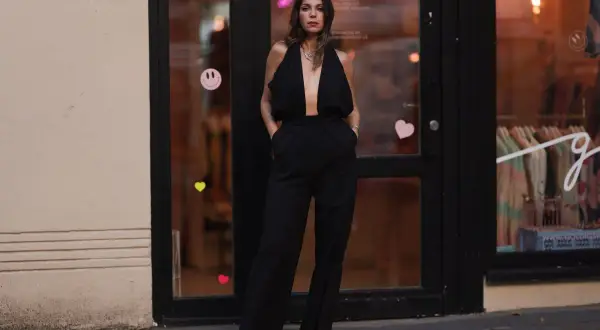 Elegancka kobieta w czarnym, głęboko wyciętym kombinezonie. Idealna inspiracja, co założyć do czarnego kombinezonu na wieczór.