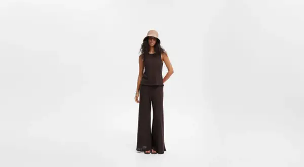 Modelka w brązowym topie i czarnych szerokich spodniach, uzupełniona kapeluszem typu bucket hat. Stylowe czarne szerokie spodnie stylizacje.