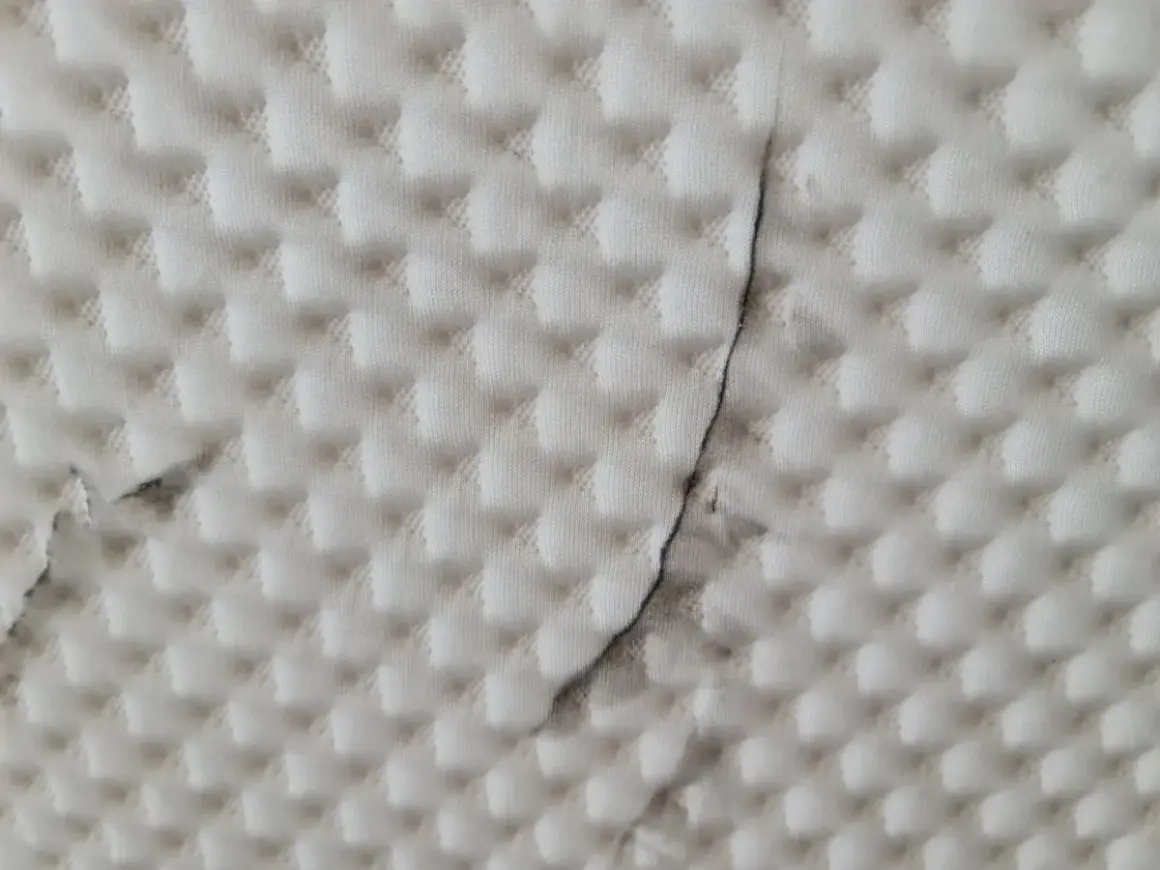 Biała tkanina z pikowanym wzorem i ciemnymi smugami.