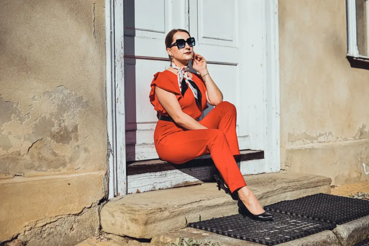 Elegancka kobieta w czerwonym kombinezonie i czarnych szpilkach. Idealne buty do czerwonego kombinezonu to klasyczne czarne czółenka.