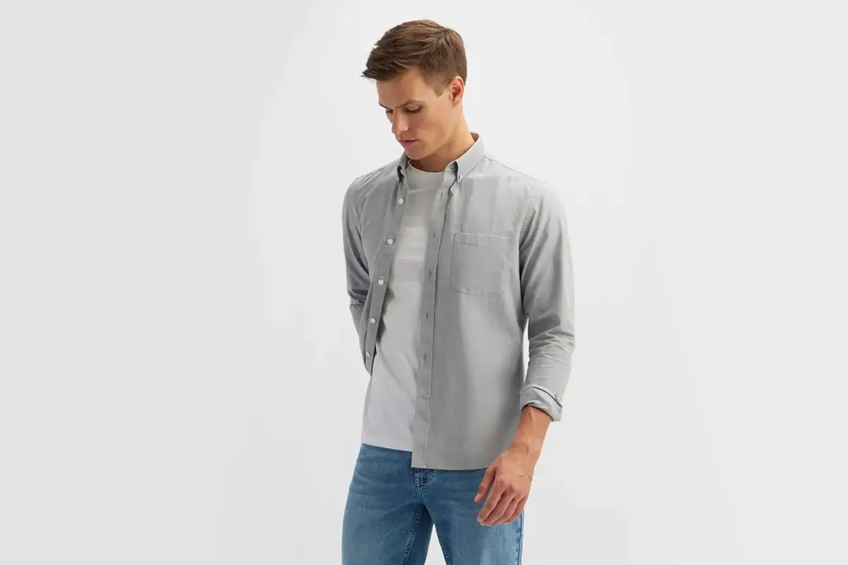 Mężczyzna w szarej koszuli i białej koszulce, dżinsach. Stylizacja smart casual.