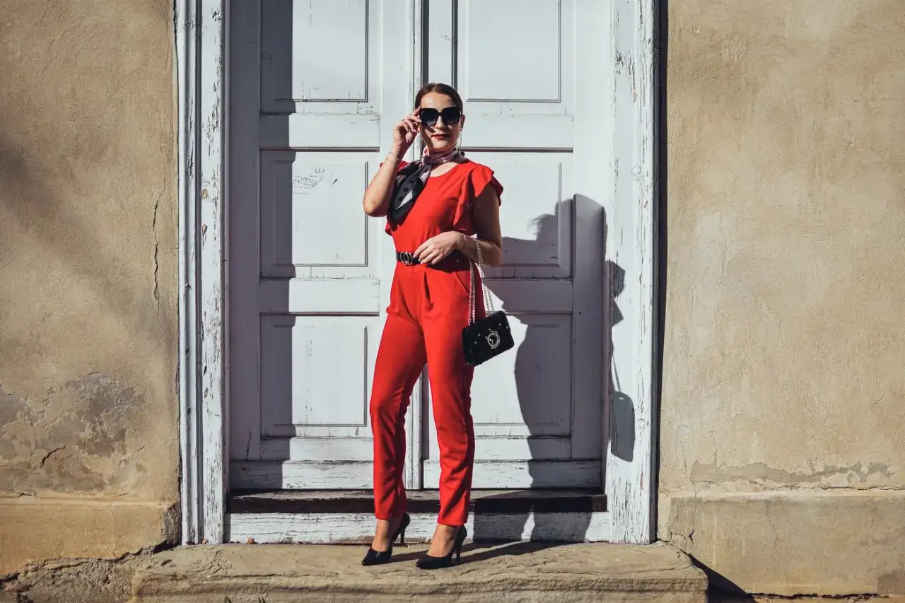 Elegancka kobieta w czerwonym kombinezonie i czarnych szpilkach. Idealne buty do czerwonego kombinezonu podkreślają stylizację.
