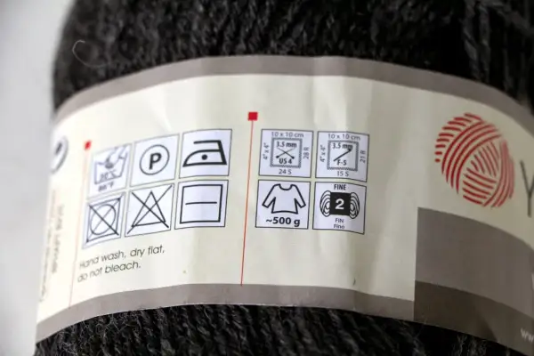 Etykieta na motku ciemnej włóczki z symbolami pielęgnacji i informacją o wadze (~500g).