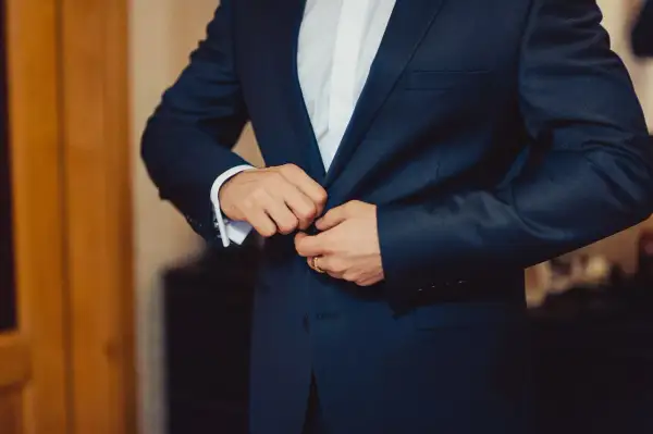 Mężczyzna zapina elegancki, granatowy **strój formalny**. Widać białą koszulę i mankiet z francuskimi spinkami.